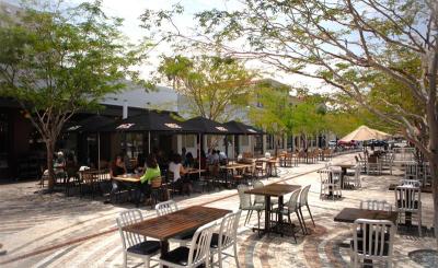 People dine in the background as sunlight pours onto a plaza with tables
